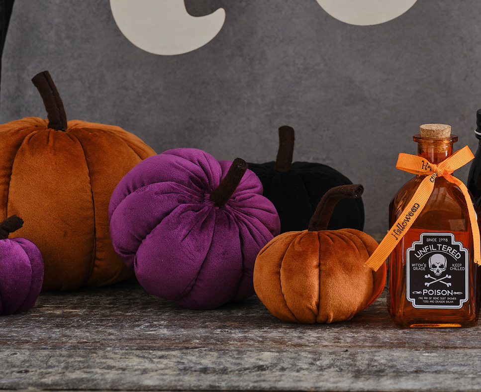 Some halloween coloured plush pumpkins sat next to an orange potion bottle