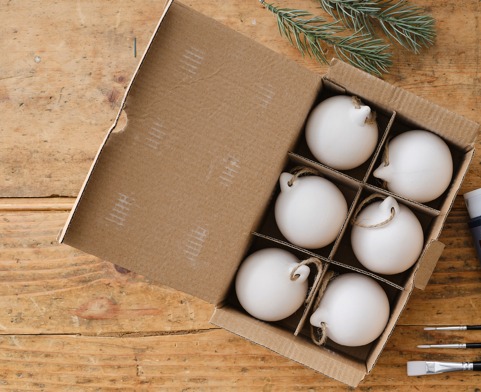 A box of six blank ceramic baubles on a wooden table