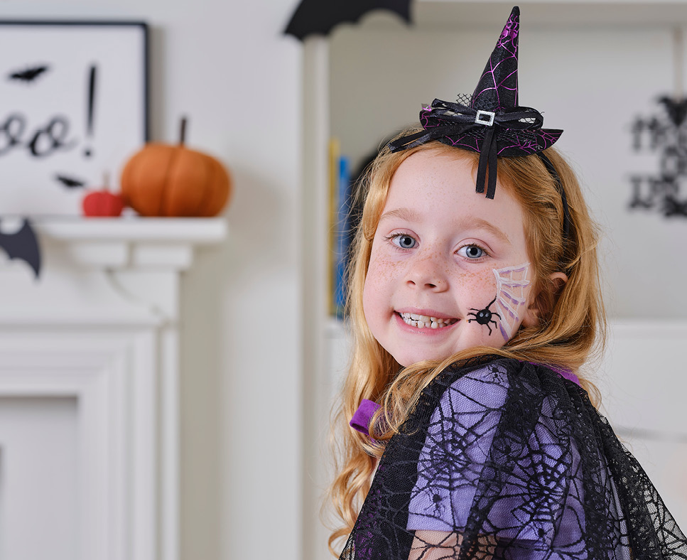 A smiling girl dressed as a witch for halloween with a spicer web painted on her face.