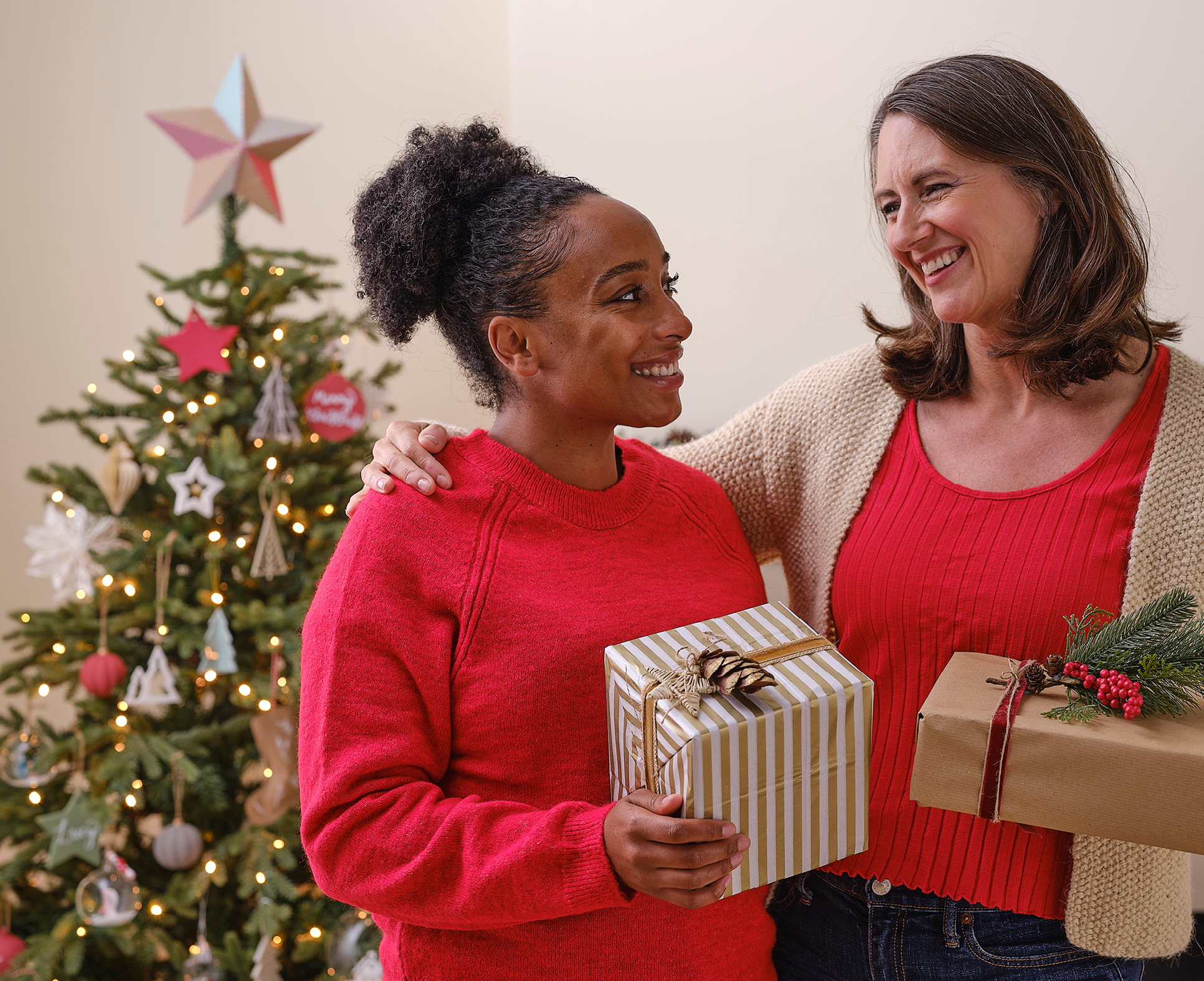 Two friends smiling, giving each other presents wrapped in Christmas themed gift wrap