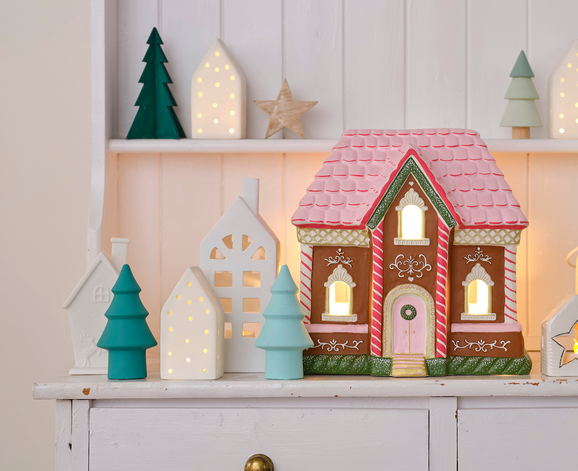 painted ceramic gingerbread house and christmas trees on a wooden table